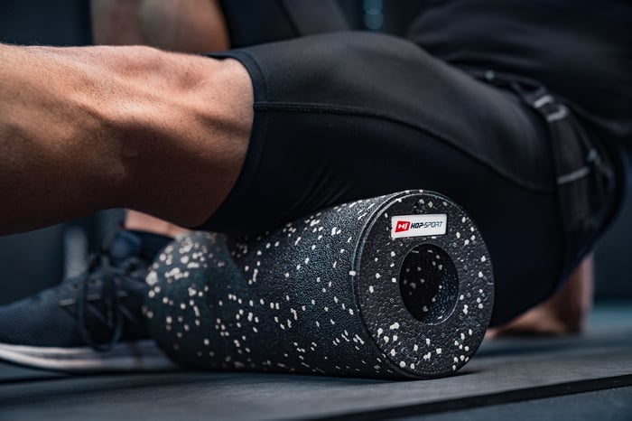 Hombre rodando los músculos de las piernas con un rodillo EPP de 33cm blanco y negro de la marca Hop-Sport