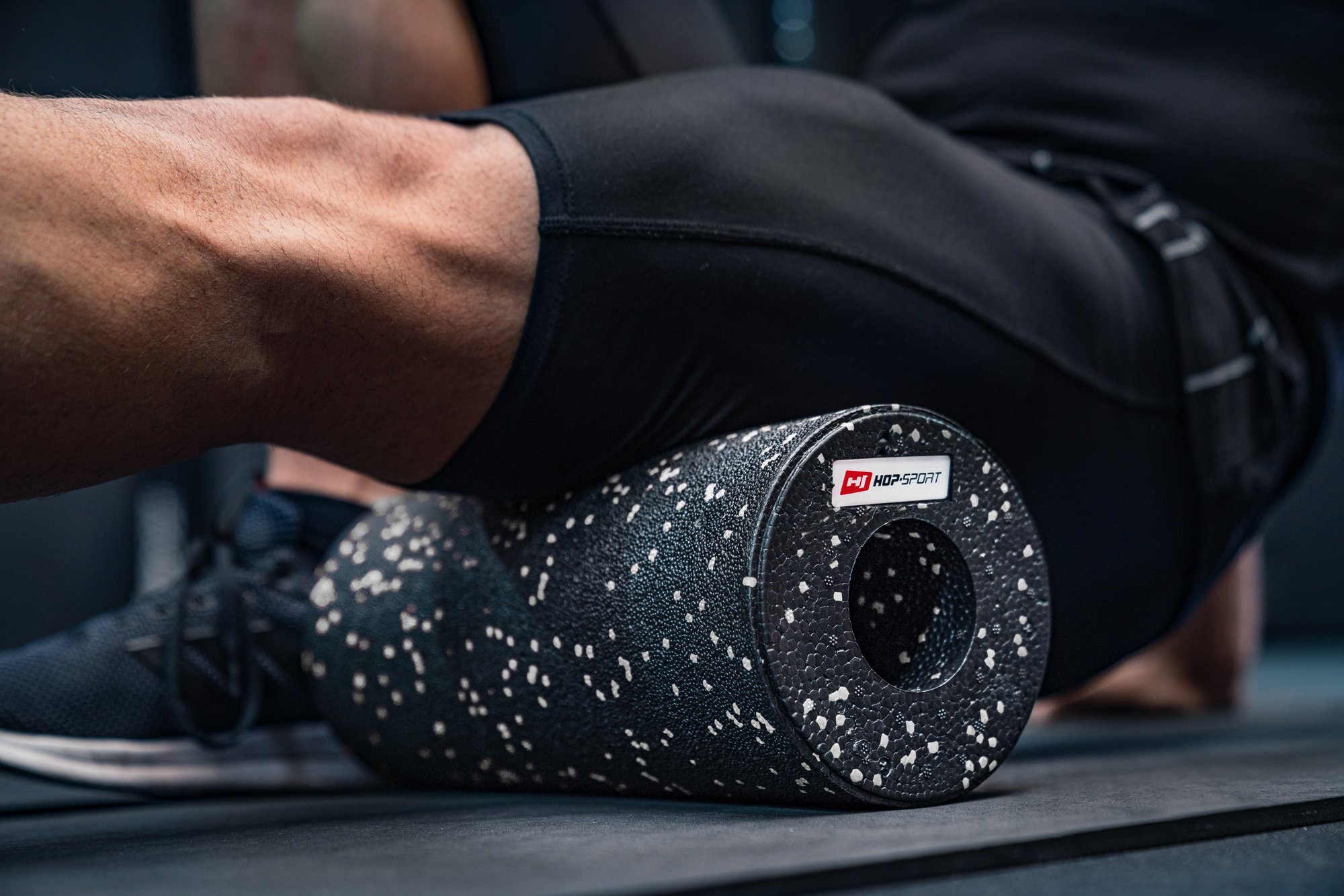 Hombre rodando los músculos de las piernas con un rodillo EPP de 33cm blanco y negro de la marca Hop-Sport