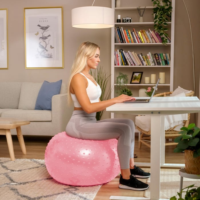 Mujer usando una pelota de gimnasia rosa con protuberancias para trabajar en el escritorio